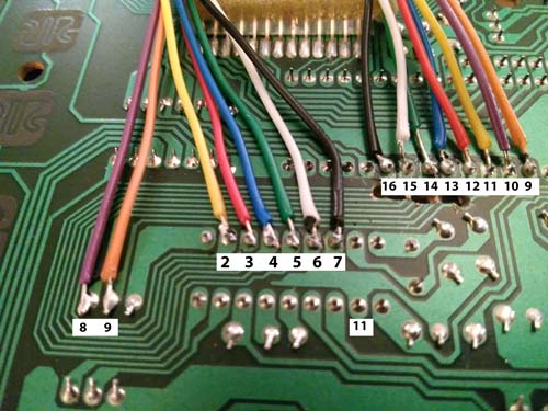 A close-up of a green printed circuit board (PCB) reveals various colored wires soldered to numbered connection points. The wires are yellow, blue, green, purple, black, orange, and white. Nearby, numbers 1 through 16 label the solder points.