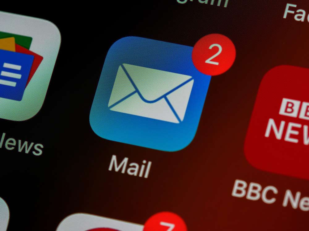 A close-up of an email app icon on a smartphone screen displays a notification indicating two unread emails. Partially visible in the background are other app icons, including Google News and BBC News.