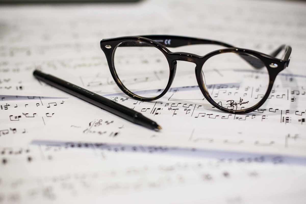 A pair of glasses and pen sit on top of music manuscript