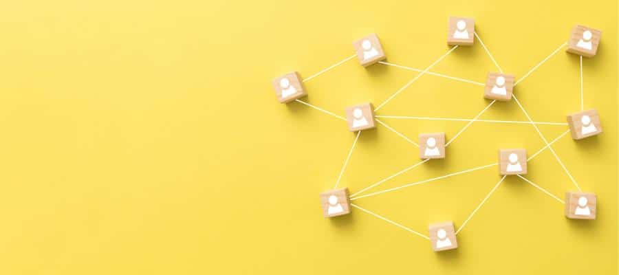 A network of small wooden blocks with user icons connected by white lines is displayed on a bright yellow background. The arrangement resembles a linked system, illustrating the concept of interconnected communication or social networking.